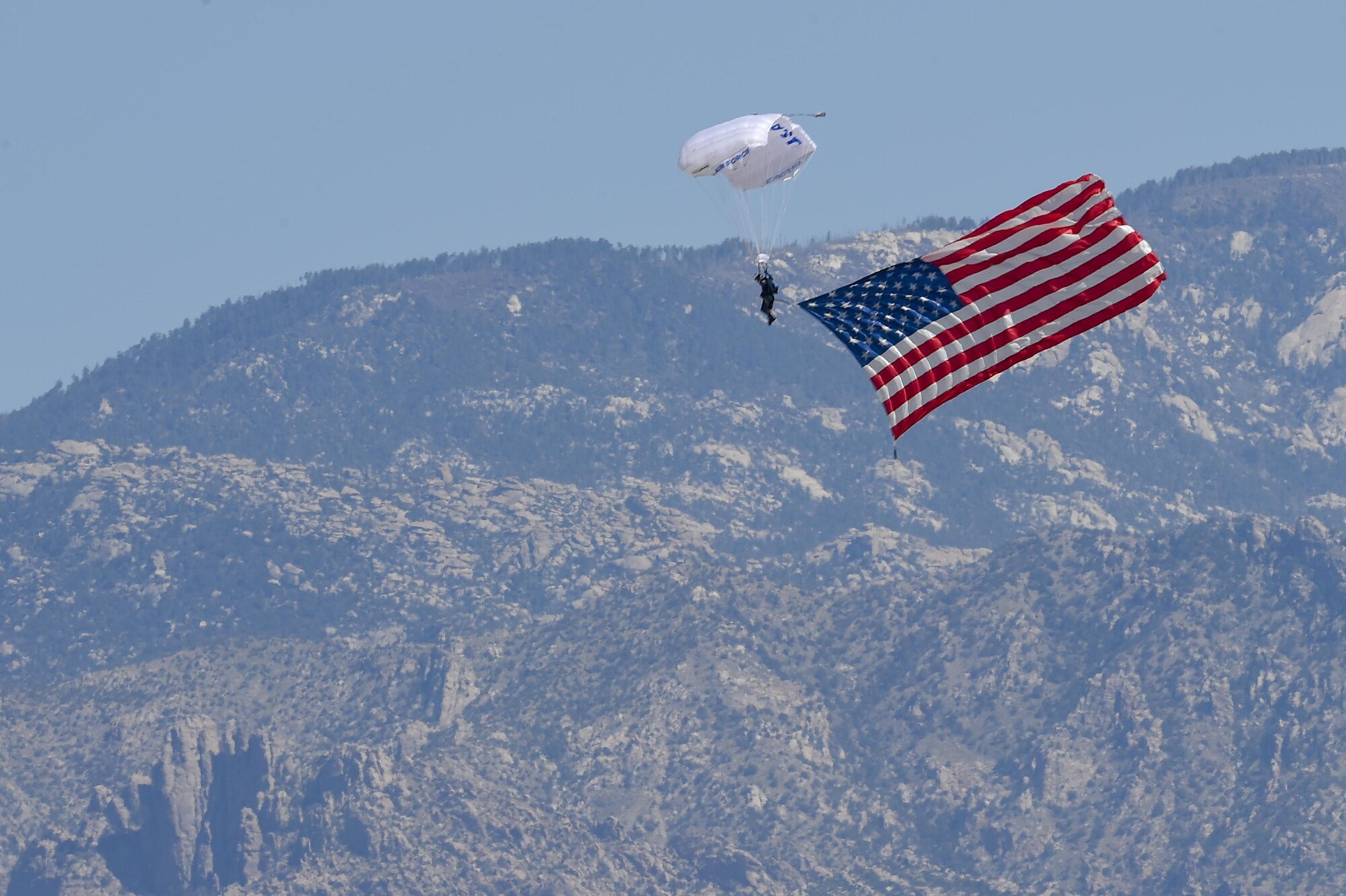 A member of the Wings of Blue U.S. Air Force Skydiving Team descends with an American Flag toward show center of the Thunder and Lightning over Arizona Open House at Davis-Monthan Air Force Base, Ariz., March 13, 2016.  The demonstration team travels across the country to airshows, sporting events, and other venues to represent the Air Force in precision parachuting. (U.S. Air Force photo by Senior Airman Chris Massey/Released) 