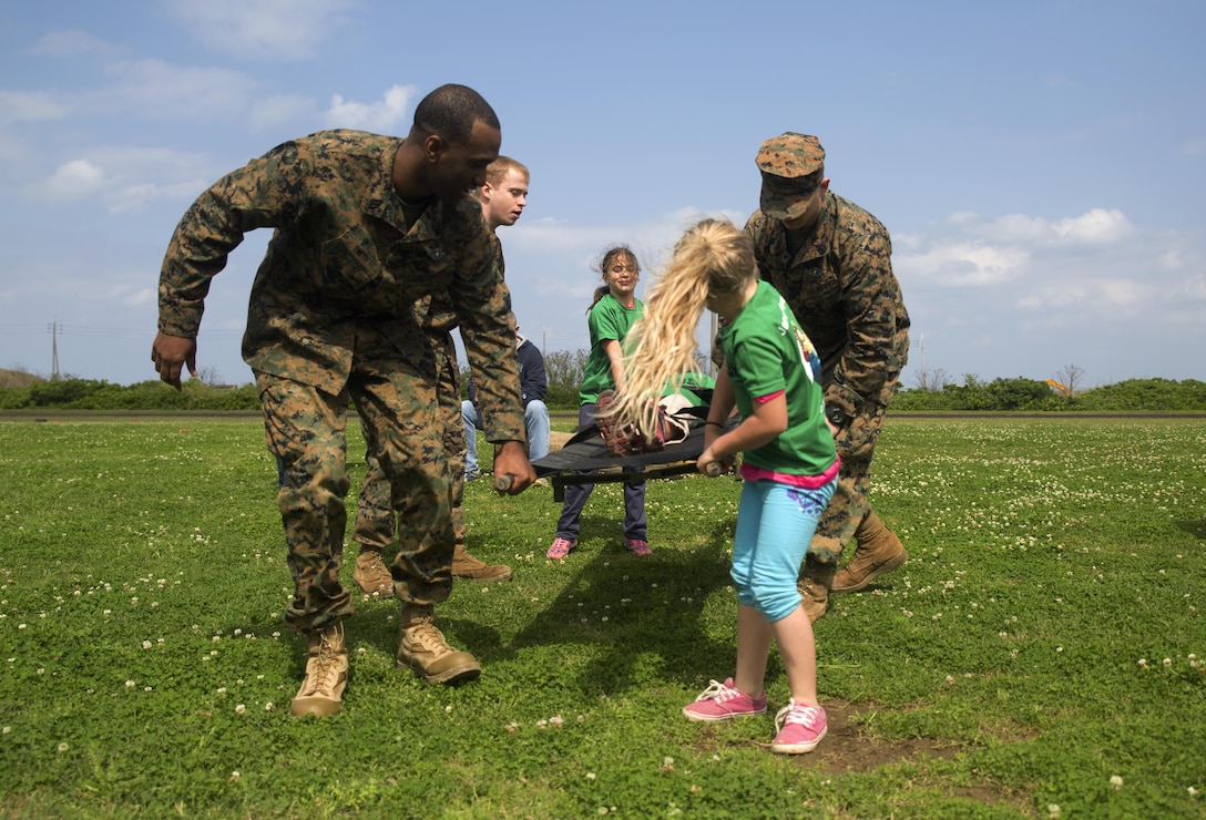 Navy corpsmen assist members of Girl Scout Troop 435 during a mock casualty evacuation during a Jane Wayne Day March 12 aboard Camp Kinser, Okinawa, Japan. Girl Scout Troop 435 attended Jane Wayne Day as a celebration of the Girl Scout Birthday. Jane Wayne Day is an event designed to allow spouses and children to gain a better understanding of some of the physical challenges military service members face. During the event, participants learned about radios, the Marine Corps Martial Arts Program, ran a modified combat fitness test, perused medical equipment and donned chemical, biological, radiological, nuclear defense equipment. The corpsmen are with Headquarters Regiment, 3rd Marine Logistics Group, III Marine Expeditionary Force.