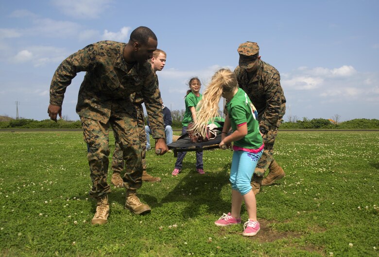 Navy corpsmen assist members of Girl Scout Troop 435 during a mock casualty evacuation during a Jane Wayne Day March 12 aboard Camp Kinser, Okinawa, Japan. Girl Scout Troop 435 attended Jane Wayne Day as a celebration of the Girl Scout Birthday. Jane Wayne Day is an event designed to allow spouses and children to gain a better understanding of some of the physical challenges military service members face. During the event, participants learned about radios, the Marine Corps Martial Arts Program, ran a modified combat fitness test, perused medical equipment and donned chemical, biological, radiological, nuclear defense equipment. The corpsmen are with Headquarters Regiment, 3rd Marine Logistics Group, III Marine Expeditionary Force.