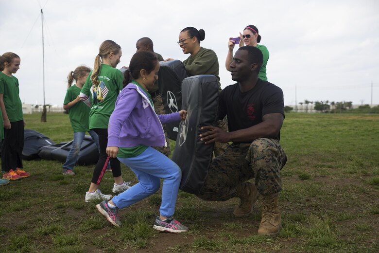 Sgt. Theophlius Bush, right, holds a kick pad for a member of Girl Scout Troop 435 during the martial arts portion of Jane Wayne Day March 12 aboard Camp Kinser, Okinawa, Japan. Jane Wayne Day provides service members with the opportunity to participate in various challenges and activities with their spouses or children. During the event, Marines and sailors demonstrated the use of radios, the Marine Corps Martial Arts Program, a modified combat fitness test, medical equipment and chemical, biological, radiological, nuclear defense equipment. Bush is a warehouse clerk with 3rd Supply Battalion, Combat Logistics Regiment 35, 3rd Marine Logistics Group, III Marine Expeditionary Force and a Jackson, Mississippi, native.