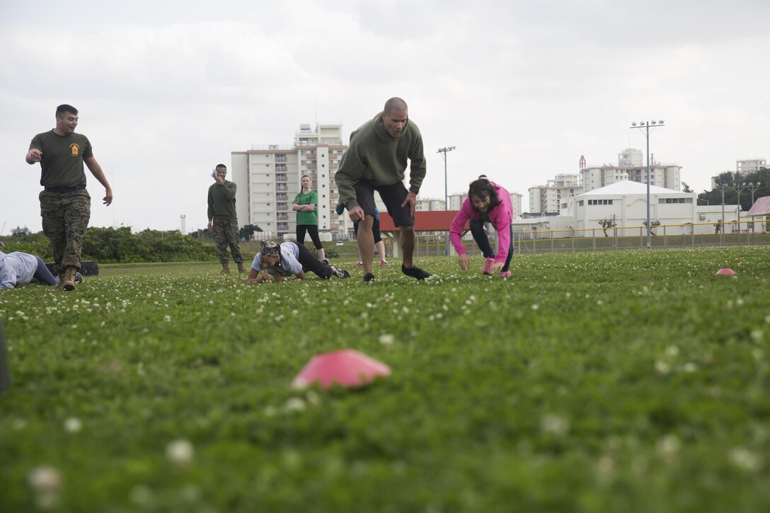 1st. Sgt. Collin D. Barry encourages a member of Girl Scout Troop 435 as she navigates her way through a modified combat fitness test during a Jane Wayne Day March 12 aboard Camp Kinser, Okinawa, Japan. Girl Scout Troop 435 participated in Jane Wayne Day, an event designed to allow spouses and children to gain a better understanding of some of the physical challenges military service members face. During the event, members of the troop learned about radios, the Marine Corps Martial Arts Program, ran a modified combat fitness test, perused medical equipment and donned chemical, biological, radiological, nuclear defense equipment. Barry is the company first sergeant of Communications Company, Headquarters Regiment, 3rd Marine Logistics Group, III Marine Expeditionary Force and a Tucumcari, New Mexico, native.