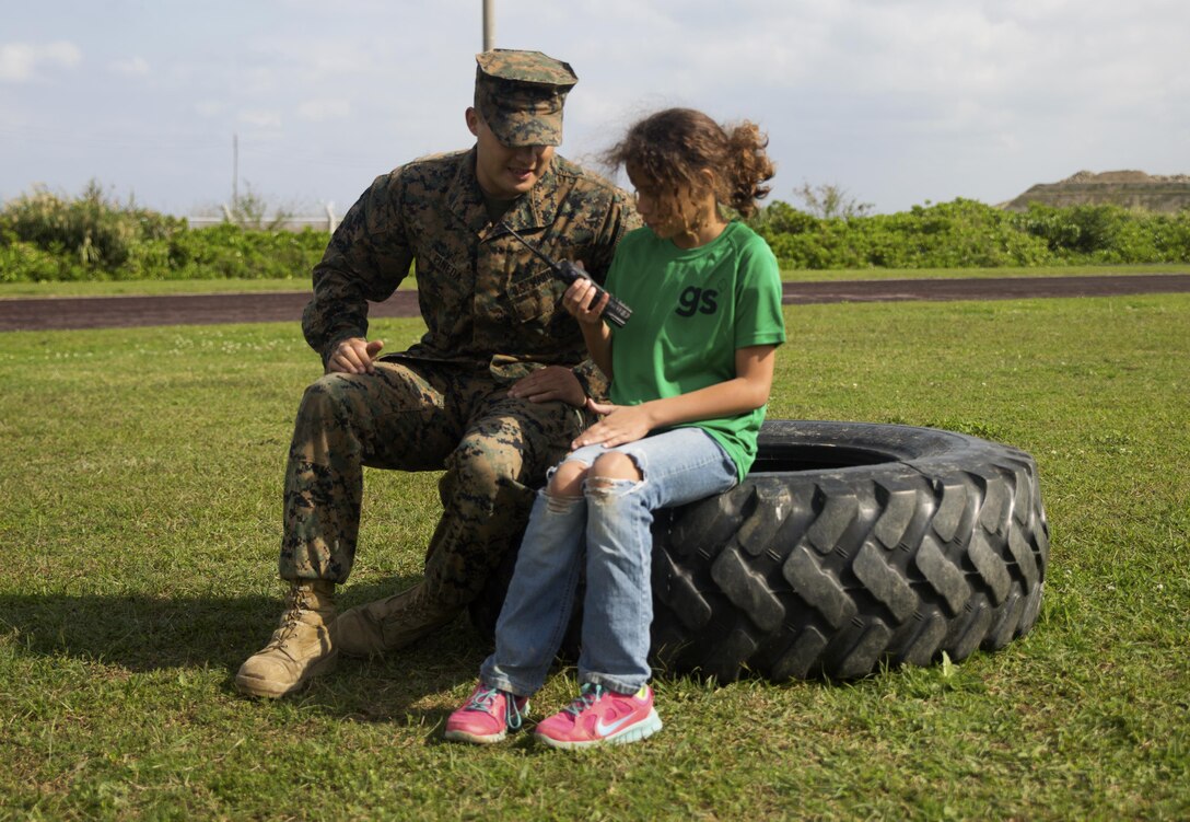 Cpl. Isaac Pineda explains radio communications to a member of Girl Scout Troop 435 during a demonstration of Marine Corps communication systems March 12 during a Jane Wayne Day aboard Camp Kinser, Okinawa, Japan. Girl Scout Troop 435 attended Jane Wayne Day to participate in various challenges and activities and gain a better understanding of some of the physical challenges military service members face. During the event, members of the troop learned about radios, the Marine Corps Martial Arts Program, ran a modified combat fitness test, perused medical equipment and donned chemical, biological, radiological, nuclear defense equipment. Pineda is a field radio operator with Communications Company, Headquarters Regiment, 3rd Marine Logistics Group, III Marine Expeditionary Force and a Cypress, California, native.