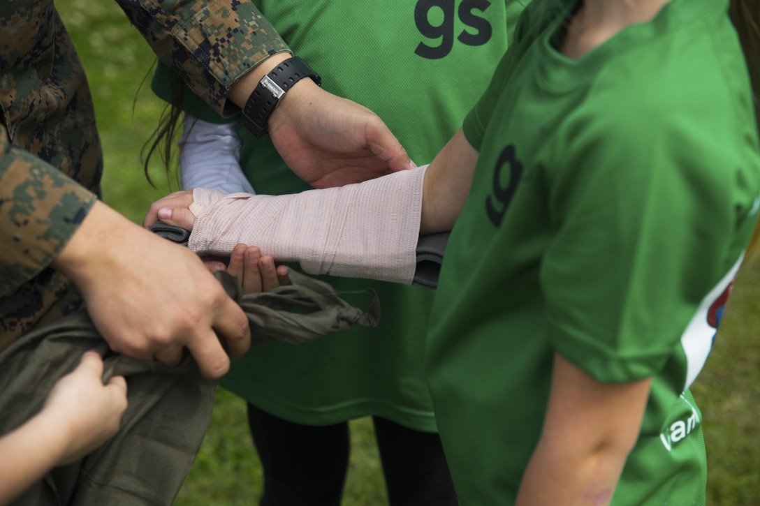 A Navy corpsman demonstrates how to splint a broken arm on a member of Girl Scout Troop 435 during a Jane Wayne Day March 12 aboard Camp Kinser, Okinawa, Japan. Jane Wayne Day is an event designed to allow spouses and children to gain a better understanding of some of the physical challenges military service members face. The troop took on the many challenges of the day as a celebration of the Girl Scout Birthday. During the event, participants learned about radios, the Marine Corps Martial Arts Program, ran a modified combat fitness test, perused medical equipment and donned chemical, biological, radiological, nuclear defense equipment.