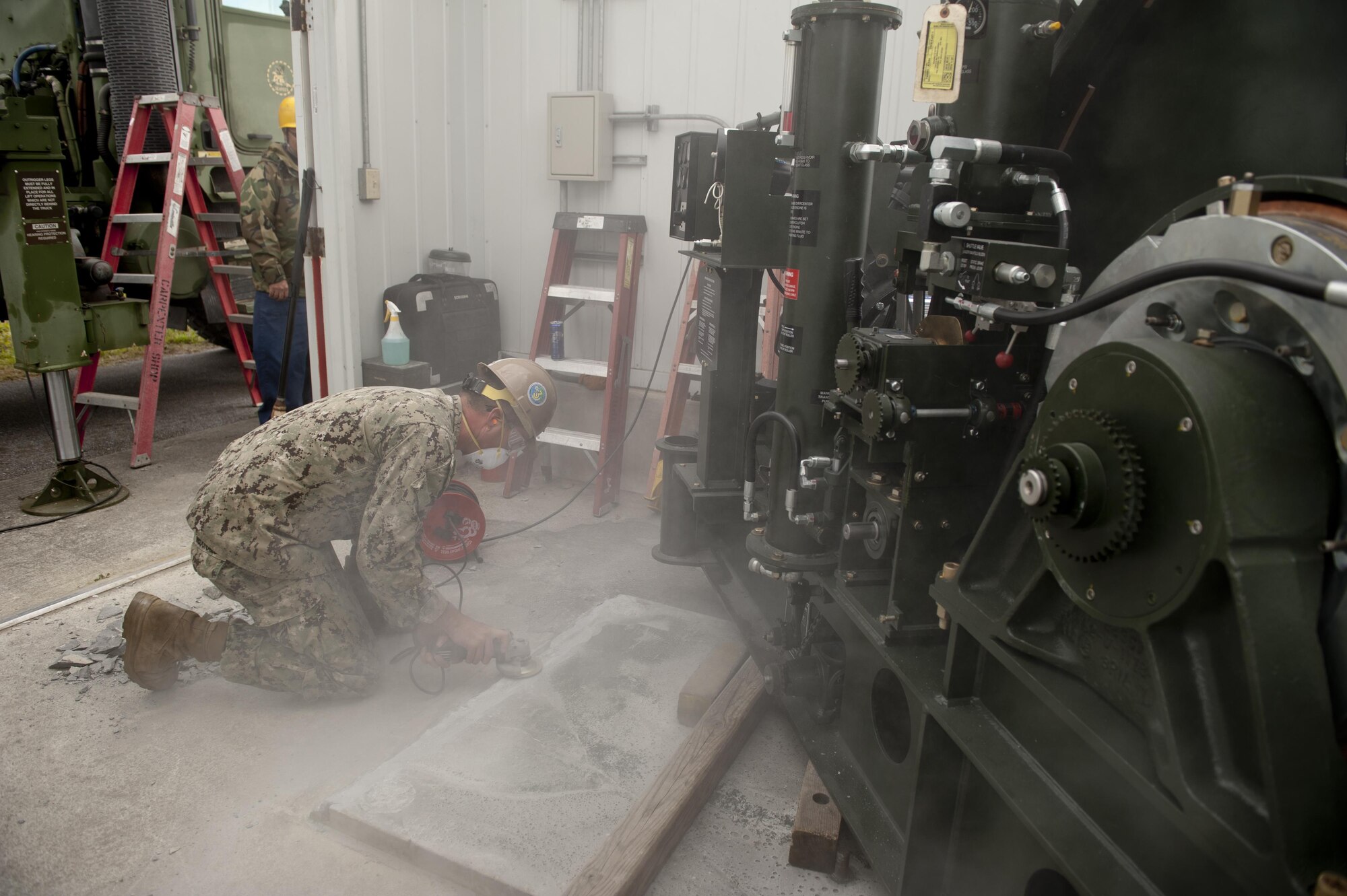 U.S. Navy Equipment Operator 2nd Class Joshua McDonald, Naval Mobile Construction Battalion 3 Seabees construction man, grinds a concrete mounting platform during aircraft arresting gear maintenance on the flight line Feb. 29, 2016, at Kadena Air Base, Japan. McDonald ensured a level mounting surface for installation of a new BAK-12 aircraft arresting system. (U.S. Air Force photo by Senior Airman Peter Reft)