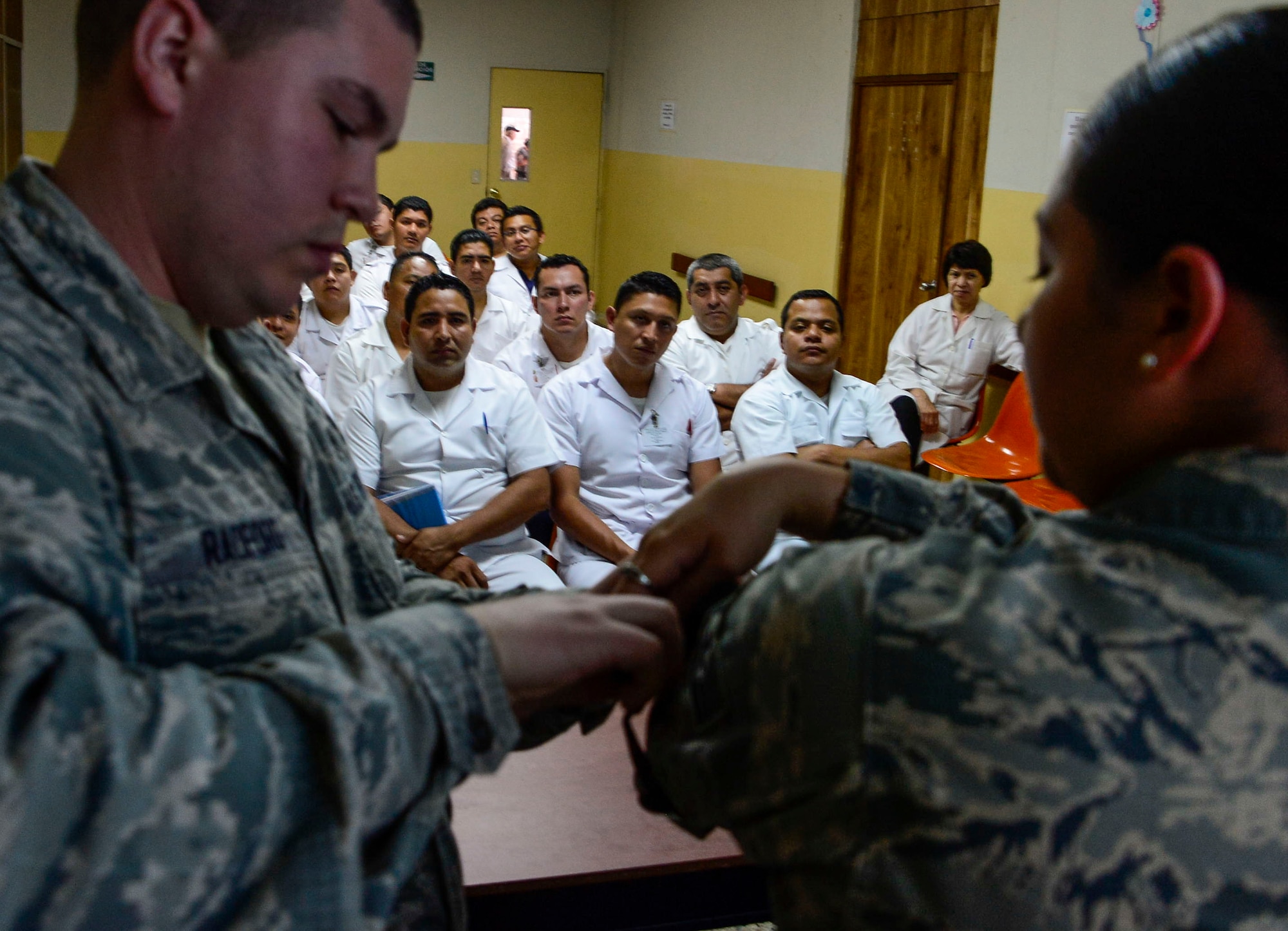 U.S. Air Force Senior Airman Jacob Radford and Staff Sgt. Karina Cortes, medical technicians stationed at Joint Base Charleston, S.C., demonstrate how to apply a tourniquet to medical technicians in training at Hospital Militar de El Salvador during a medical subject matter expert exchange in San Salvador, El Salvador, March 11, 2016. Earlier in the week, Carey led a team of Air Force medical professionals in a week-long exchange with Salvadoran medics at Ilopango Air Base. After the subject matter expert exchange was completed, the team was invited to a share their expertise with members of the Hospital Militar de El Salvador. (U.S. Air Force photo by Tech. Sgt. Heather R. Redman/Released)