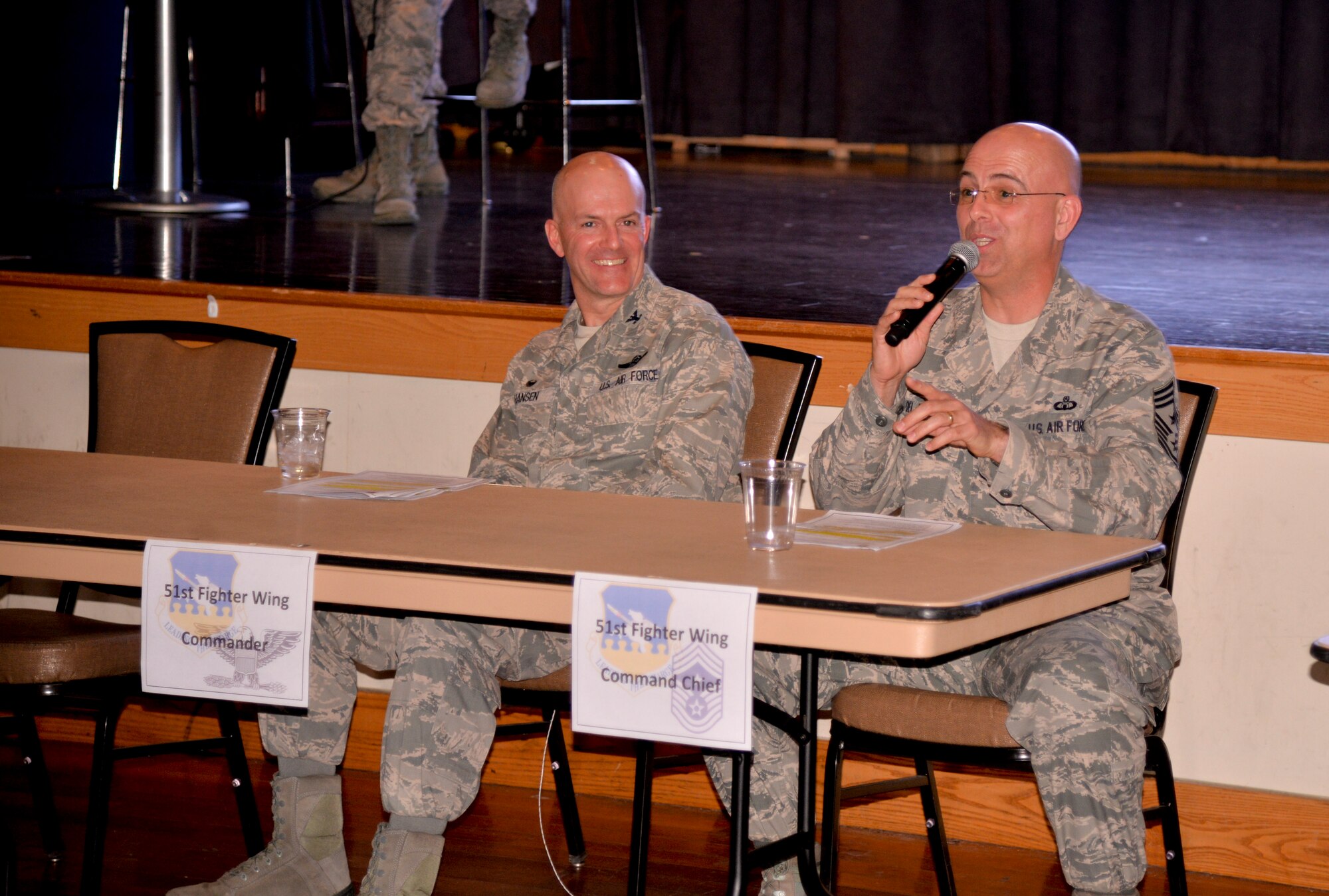 Col. Andrew Hansen, 51st Fighter Wing commander, looks on as Chief Master Sgt. Alex Del Valle, 51st FW command chief, speaks during a combined live and social media town hall meeting March 15, 2016, at Osan Air Base, Republic of Korea. Leadership from across base came out to the event in order to provide advice and assistance to members of Team Osan who had questions or concerns. (U.S. Air Force photo Staff Sgt. Benjamin Sutton/Released)