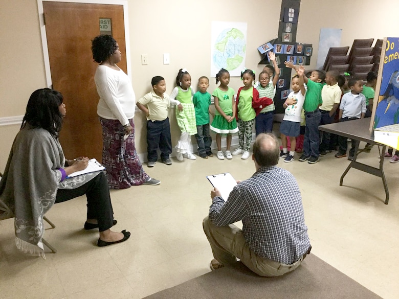 Contracting Officer Dr. K.T. Johnson and Steven Pautz, center closeout manager, talk to Ms. Perkin's kindergarten class about their group project during the First Baptist Child Development Center & Academyscience fair.