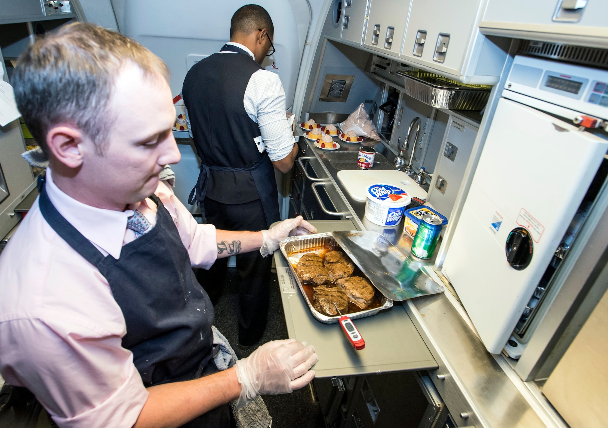 Tech. Sgt. Albert Meriano III and Staff Sgt. Casey Watson, 1st Airlift Squadron flight attendants, prepare lunch at about 50,000 feet while in flight to Royal Air Force Mildenhall, England, Oct. 10, 2015. While a flight attendant’s primary duties is the safety of passengers, they are also culinary artists and experts with customs regulations. (U.S. Air Force photo/Senior Master Sgt. Kevin Wallace)