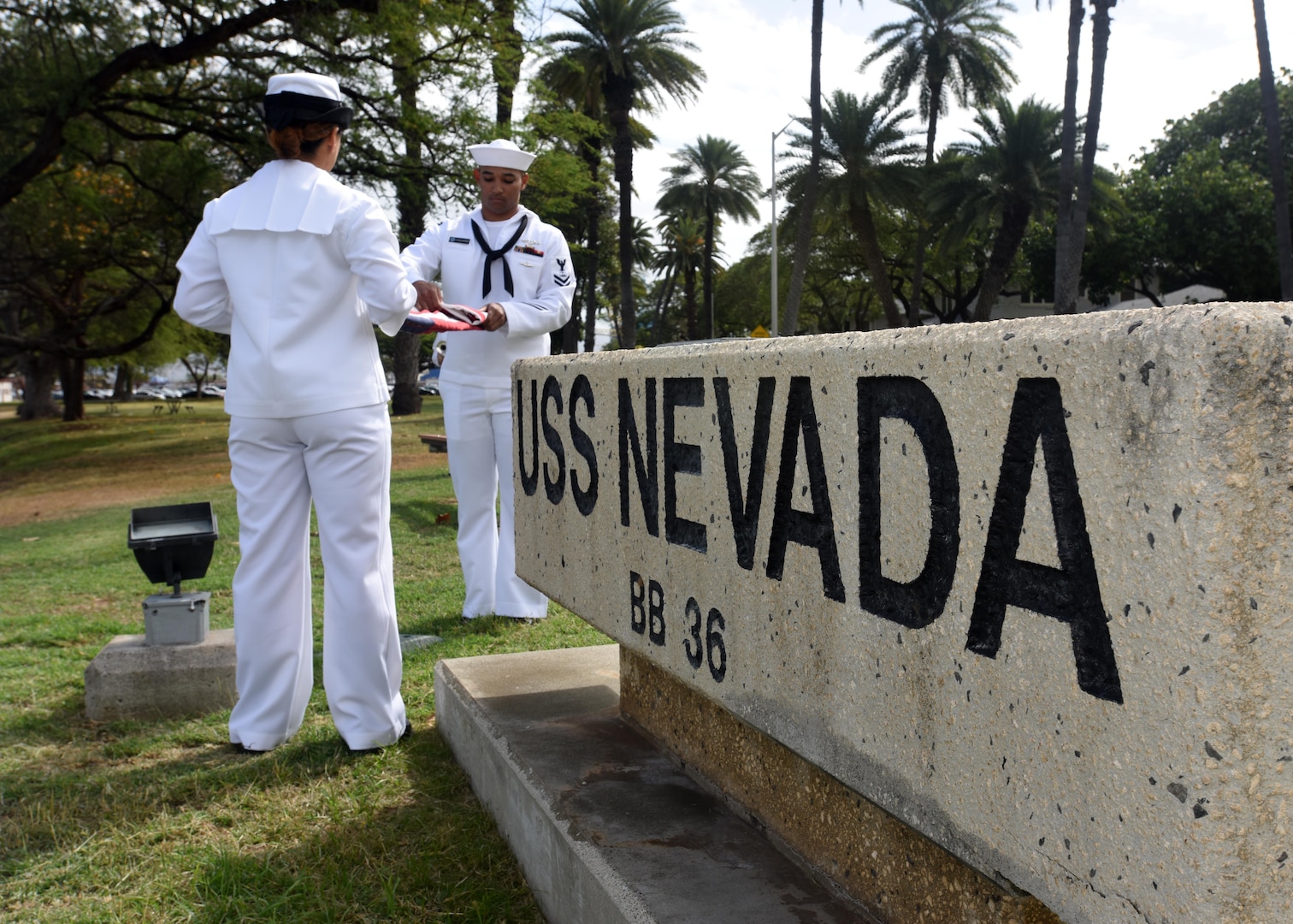 160311-N-QL961-111 PEARL HARBOR (Mar. 11, 2016) Operations Specialist 3rd Class Jasmine Bencid, left, and Culinary Specialist 2nd Class David Johnson, both members of the Joint Base Pearl Harbor-Hickam (JBPHH) color guard, fold the national ensign during a commemoration ceremony for the USS Nevada (BB 36) 100th anniversary of its commissioning at the USS Nevada memorial on JBPHH. The ceremony was conducted at the Nevada memorial simultaneously as a similar ceremony was being held in Carson City, Nevada. (U.S. Navy photo by Mass Communication Specialist 1st Class Phillip Pavlovich/Released)