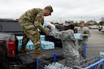Maj. George Hurd, left, Staff Sgt. Erdoo Thompson, center, and 1st Lt. Matthew Verdugo, right, all of the 136th Maneuver Enhancement Brigade, load bottled water in preparation for Hurd's convoy to Flint, Michigan, March 10, 2016, in Round Rock, Texas. 