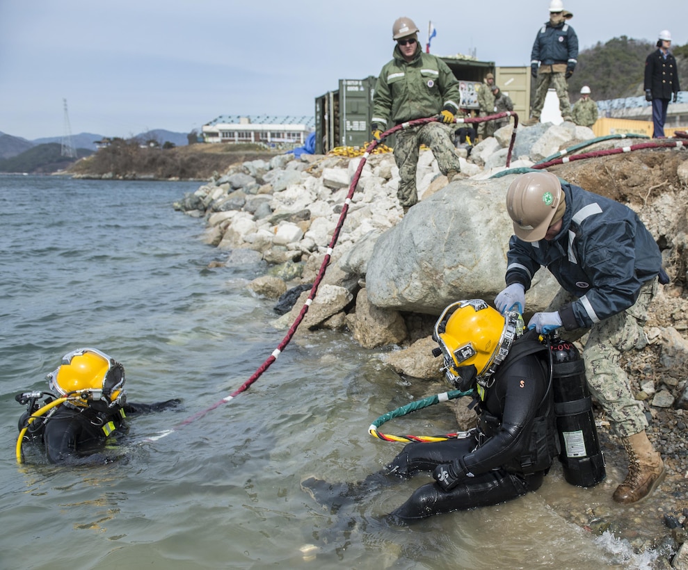 U.S. Navy Petty Officer 2nd Class Zachary Schulte, right, pours warm water into the wet suit of South Korean Chief Petty Officer Dong Soon-jung as the divers take a break from working on a simulated expeditionary wharf during Exercise Foal Eagle 2016 at Chinhae, South Korea, March 10, 2016. Schulte is a builder assigned to Underwater Construction Team 2. Navy photo by Petty Officer 1st Class Charles E. White