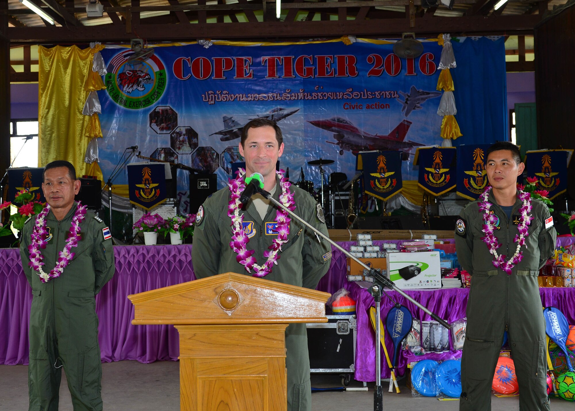 Group Captain Manoon Rukitna, exercise director for the Royal Thailand Air Force (left) and Col. Sim Pengshin, exercise director from the Republic of Singapore Air Force, (right) stand by as Col. Jack Arthaud, exercise director for the U.S. Air Force, addresses students, school faculty, and military members attending a combined civic action engagement during Exercise Cope Tiger 16, Thong Chai Wittaya Primary School, Korat, Thailand, March 15, 2016. The combined civic action engagement provides an outlet for the countries participating in Cope Tiger to give back to the community surrounding Korat Royal Thai Air Force Base. Exercise Cope Tiger is multilateral field training exercise and includes more than 1,200 personnel from the United States, Thailand and Singapore. The purpose of this exercise is to improve readiness and interoperability between three countries and continue the growth of strong relationships within the Asia-Pacific Region. (U.S. Air Force Photo by Tech Sgt. Aaron Oelrich/Released)