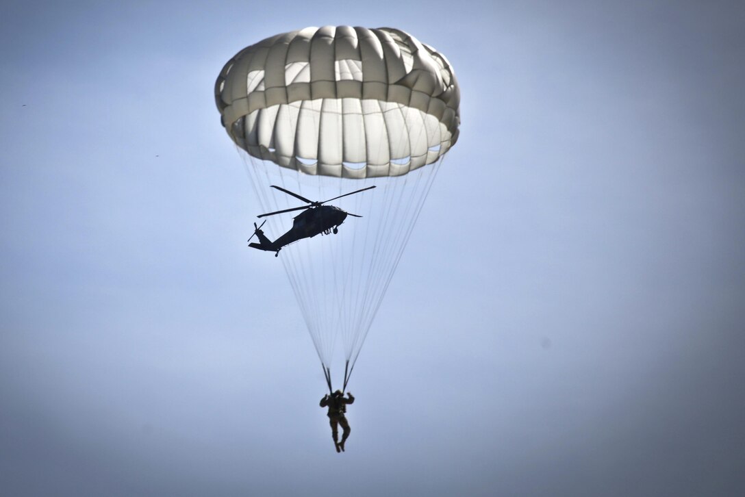 A paratrooper descends in his T-10 parachute as a UH-60 Black Hawk helicopter prepares to deploy more paratroopers during parachute jump training over Coyle drop zone on Joint Base McGuire-Dix-Lakehurst, N.J., March 12, 2016. New Jersey Air National Guard photo by Tech. Sgt. Matt Hecht