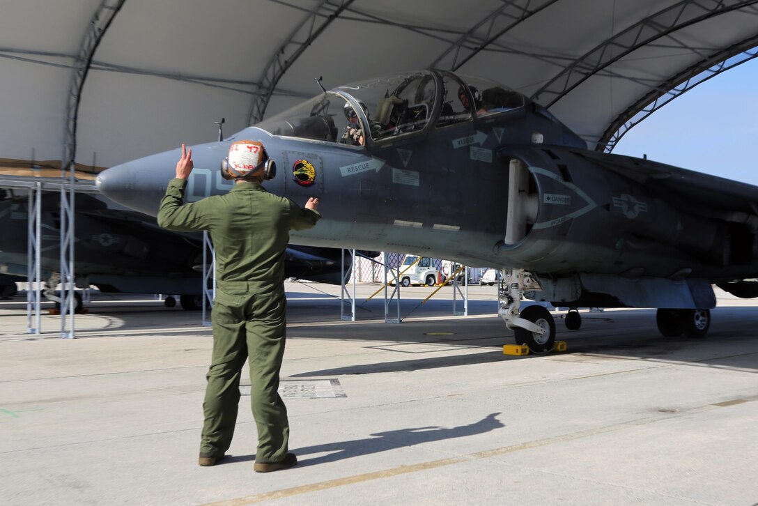 A plane captain communicates with the crew of an TAV-8B Harrier pilot prior to take off at Marine Corps Air Station Cherry Point, N.C., March 11, 2016. A plane captain is responsible for conducting a final examination of the aircraft and guiding the pilots out onto the runway. Plane captains possess extensive knowledge of their designated aircraft and can determine if there are any last minute discrepancies that could potentially ground the aircraft. (U.S. Marine Corps photo by Cpl. N.W. Huertas/Released)