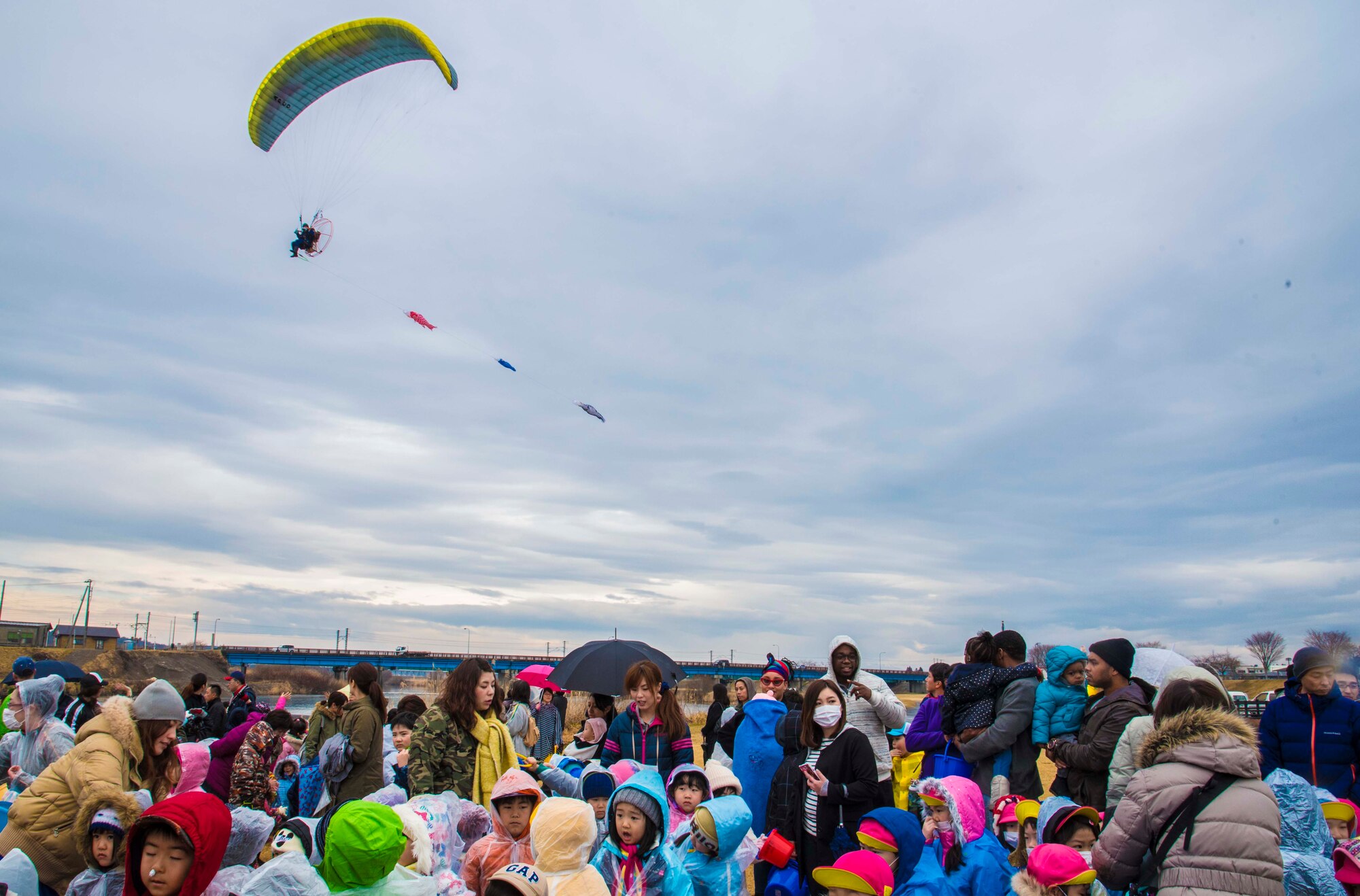 A powered parachutist flies over a group of spectators at the Oirase Salmon Park, Japan, March 19, 2016. More than 400 people from the local area and Misawa Air Base attended the 19th Annual Baby Salmon Release to place the fish in the Oirase River, ensuring the salmon life cycle continues. (U.S. Air Force photo by Airman 1st Class Jordyn Fetter)