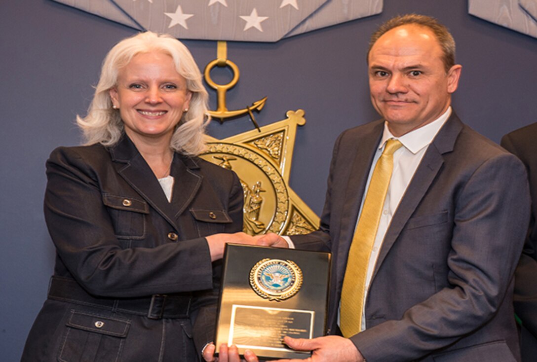 Ms. Kristen Baldwin, acting deputy assistant secretary of defense, systems engineering (left) presents an award for achievement in defense standardization to John Bonitatibus, electronics engineer at Defense Logistics Agency Land and Maritime inside the Hall of Heroes at the Pentagon, March 16, 2016.