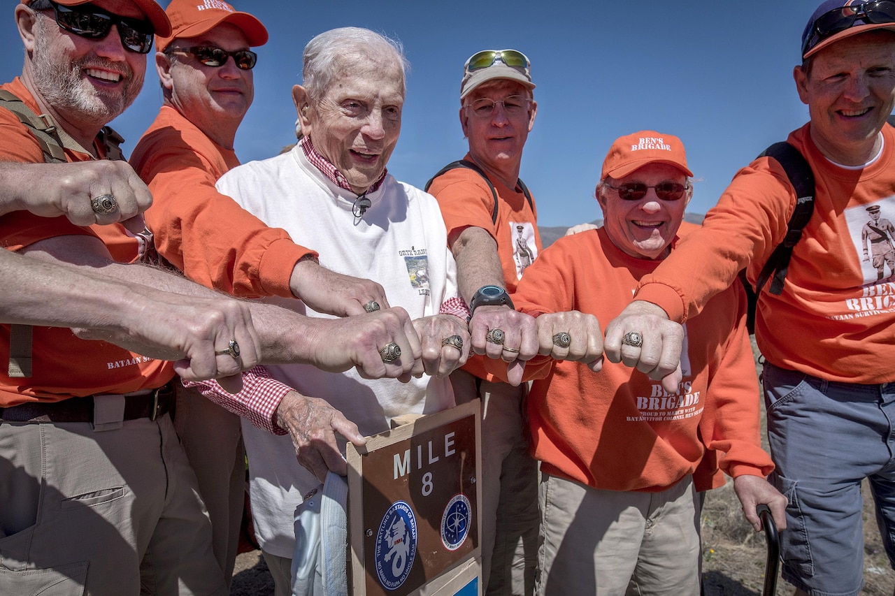 A veteran and a group of marchers in orange shirts hold out their fists to display class rings.