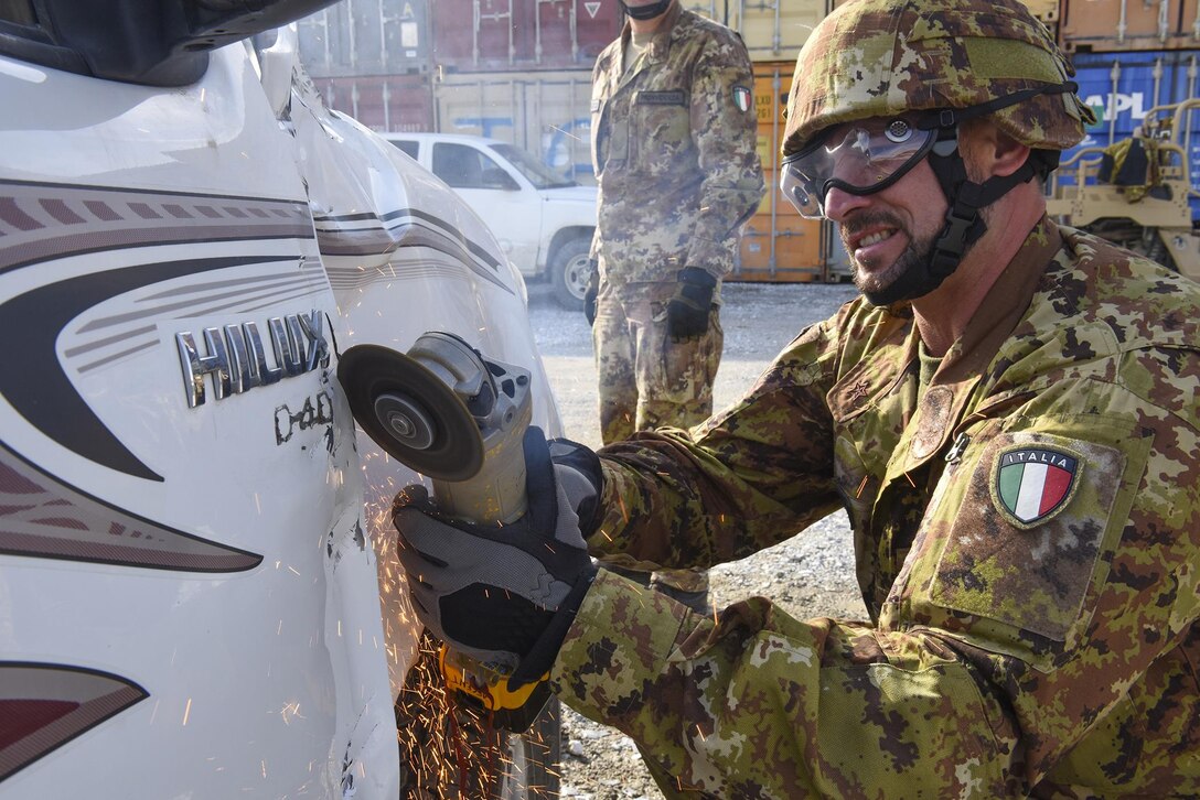 An Italian soldier uses a grinder to cut the hinges off of a truck door during combined extrication training with U.S. airmen at Bagram Airfield, Afghanistan, March 19, 2016. Air Force photo by Capt. Bryan Bouchard