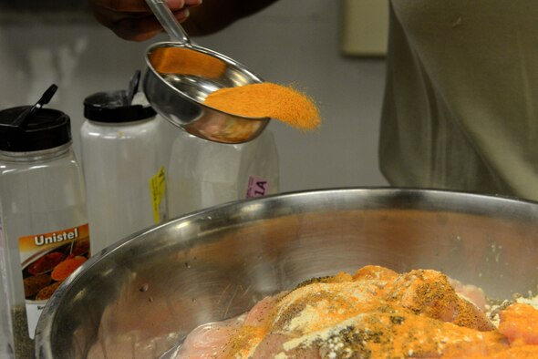 U.S. Air Force Airman 1st Class Treasure Jacobs, 20th Force Support Squadron services apprentice, pours seasoning onto chicken at the Chief Master Sgt. Emerson E. Williams Dining Facility on Shaw Air Force Base, S.C., March 17, 2016. The dining facility plans meals according to a 21-day meal schedule provided by the U.S. Air Force. (U.S. Air Force photo by Airman 1st Class Destinee Dougherty)