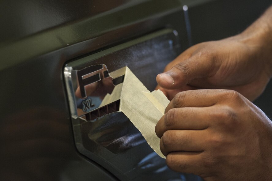U.S. Air Force Staff Sgt. Phillip Robinson, 23d Logistics Readiness Squadron vehicle maintenance journeyman, removes tape from a recently painted vehicle, March 22, 2016, at Moody Air Force Base, Ga. Among repairs and routine maintenance, the 23d LRS applies a fresh coat of paint to vehicles in order to maintain their value. (U.S. Air Force photo by Airman 1st Class Lauren M. Johnson/Released)