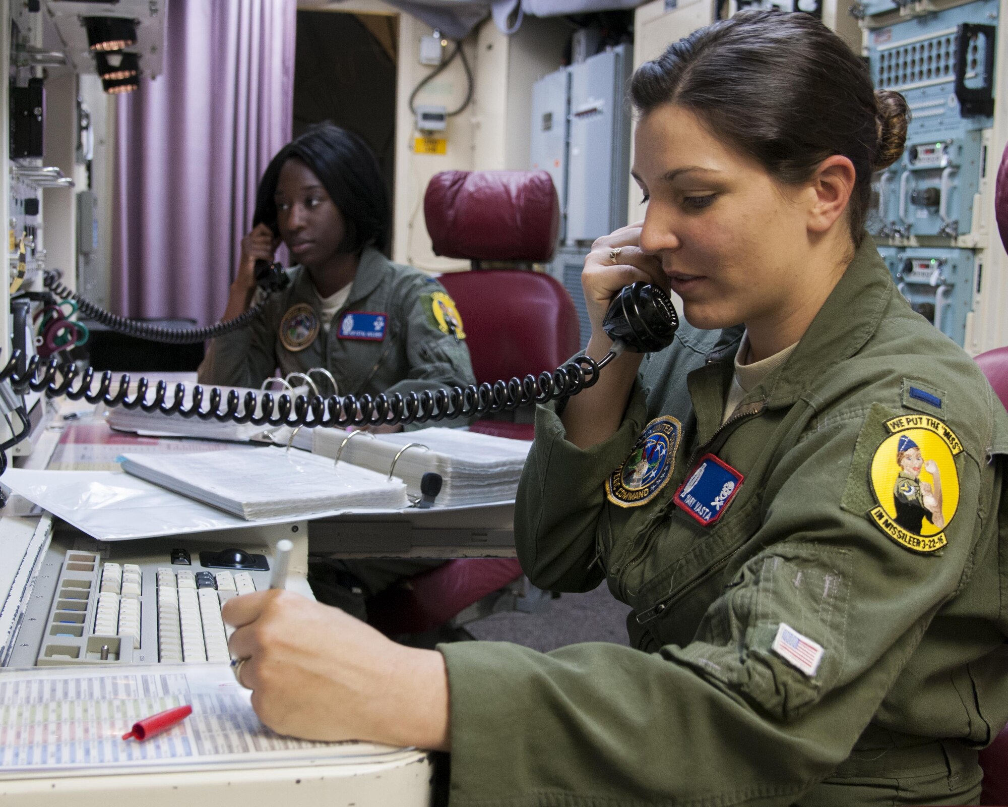 1st Lt. Mary Vasta, 319th Missile Squadron combat crew commander, and 1st Lt. Krystal Wilder, 319th MS combat crew deputy, speak on phones in a launch control center, March 22, 2016, in the F.E. Warren Air Force Base, Wyo., missile complex. Female officers participating in the all-female alert wore specialized badges to commemorate the event. (U.S. Air Force photo by Airmen 1st Class Malcolm Mayfield)