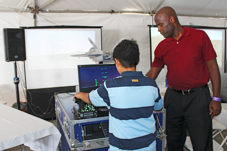 Kelvin Verrett, 412th Test Engineering Group, shows a young spectator the group's traveling F-22 simulator during the L.A. County Air Show March 20. The air show had a large science, technology, engineering and math area to promote STEM programs throughout the local area. (U.S. Air Force photo by Melissa Buchanan)