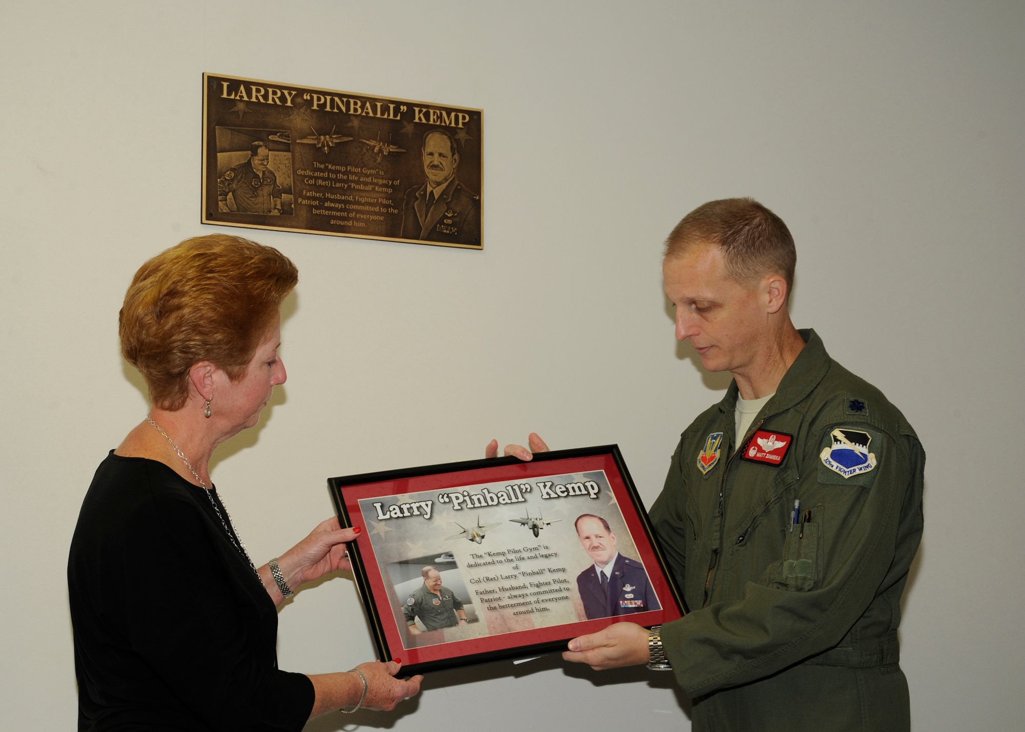 Adelina Kemp, (left) is presented a lithograph of Col. Larry “Pinball” Kemp by Lt. Col. Matthew Zamiska, 325th Training Support Squadron commander, March 21, at the newly named Kemp Pilot Gym. The event commemorated the gym to Col. Kemp. (U.S. Air Force photo by Senior Airman Solomon Cook/Released)