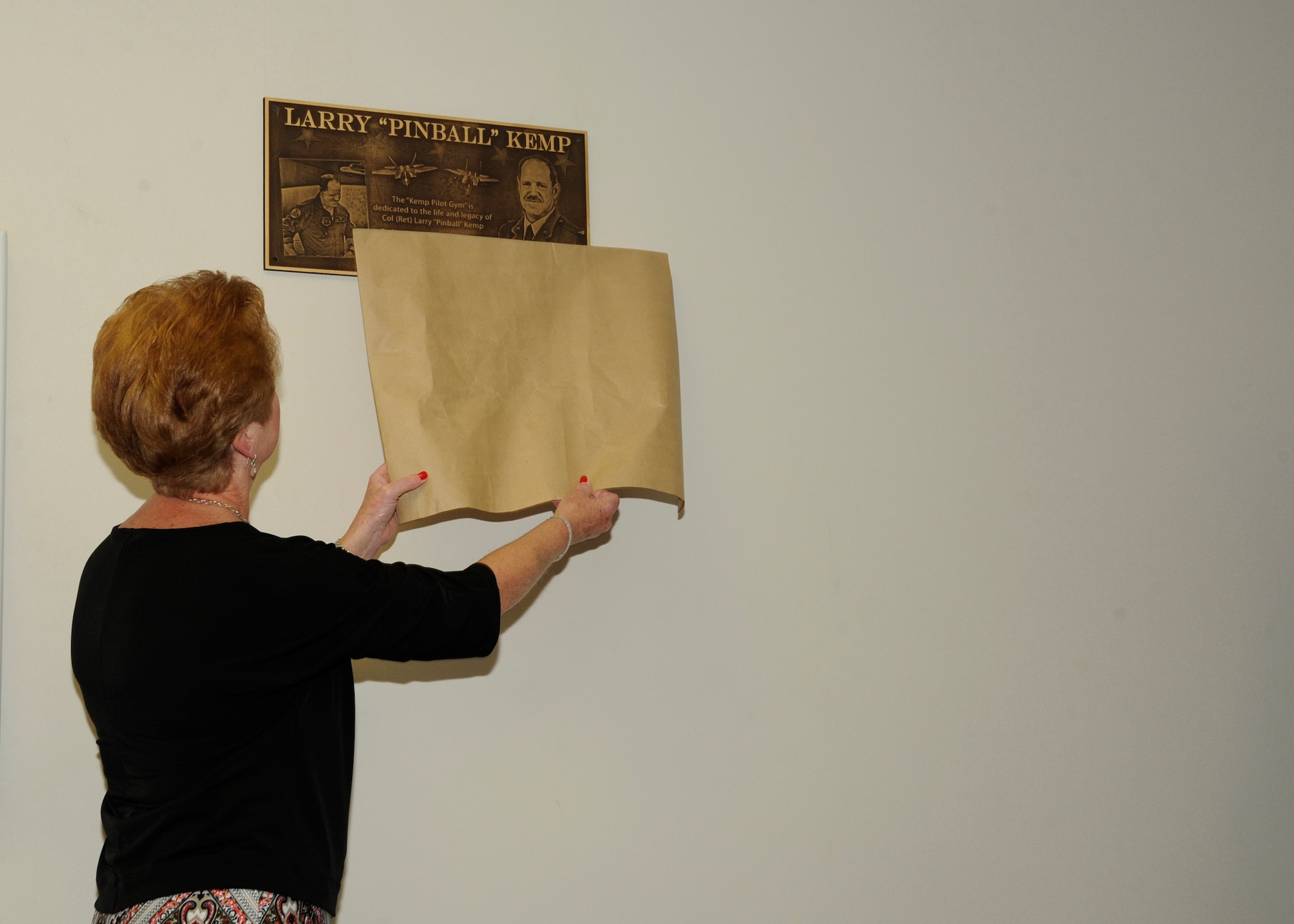 Adelina Kemp, unveils a plaque of the newly named Kemp Pilot Gym March 21, at Tyndall, Air Force Base, Fla. The purpose of this event was to dedicate the gym to the memory of Col. Larry “Pinball” Kemp. (U.S. Air Force photo by Senior Airman Solomon Cook/Released)