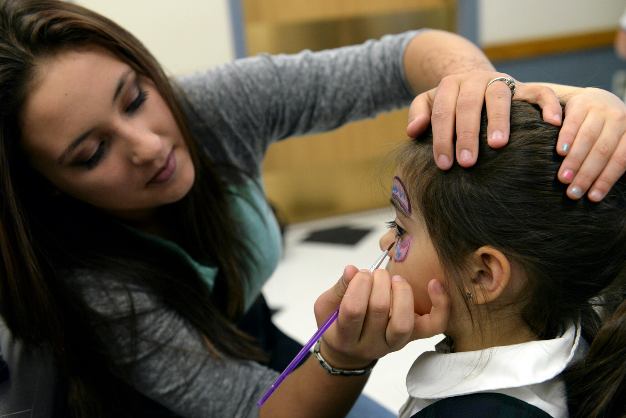 Jessie Jelsma paints an Easter design on Isabella Bowers’s face during an Air Force family dinner March 23 at the Hill Air Force Base chapel. The dinner, hosted by the Air Force Sergeants Association, Chapter 1163, provided a stress-free meal and entertainment to family members whose Airmen spouses and parents are currently deployed. More than 30 Airmen from the base’s Airman Leadership School volunteered to support the event, providing food and serving families. (U.S. Air Force photo by Paul Holcomb) 