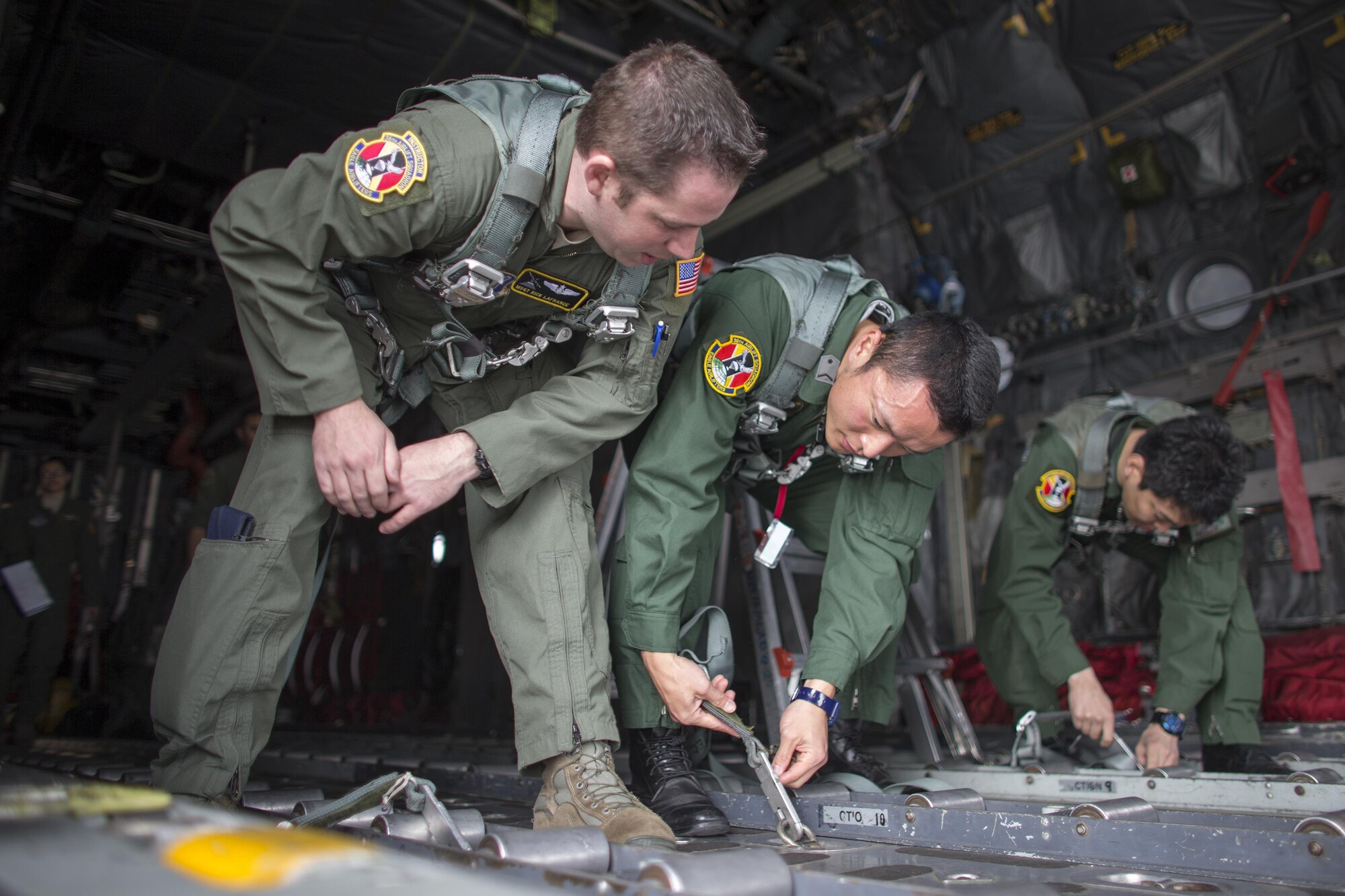 (Left to right) U.S. Air Force Master Sgt. Richard LaFrance, 36th Airlift Squadron C-130 loadmaster, instructs Japan Air Self-Defense Force Staff Sgt. Naoto Ishii, 403rd Tactical Airlift Squadron C-1 loadmaster, and JASDF Tech. Sgt. Suguru Yahata, Special Airlift Group B747 loadmaster, on how to secure a harness at  Yokota Air Base, Japan, March 23, 2016, during non-commission officer exchange program. Yokota hosted sixteen JASDF NCO members in various work-places for nine days. (U.S. Air Force photo by Osakabe Yasuo/Released)