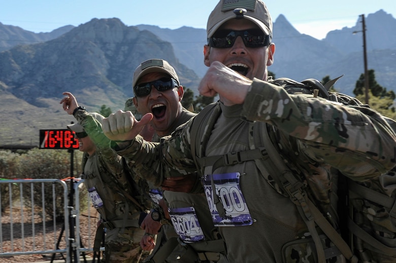 Peruvian Air Force exchange Officer Maj. Javier Camacho, center, and U.S. Air Force 1st Lt. Corbin Aldridge, 19th Logistics Readiness Squadron aerial port flight commander, cross the finish line of the 27th annual Bataan Memorial Death March, at White Sands Missile Range, N.M., March 20, 2016. The 19th LRS team completed the World War II memorial ruck march in less than nine hours. (U.S. Air Force photo by Senior Airman Harry Brexel)