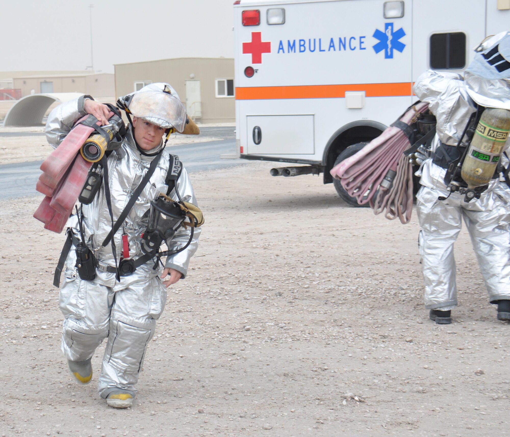 Staff Sgt. Gregory Mazzone, 379th Expeditionary Civil Engineer Squadron firefighter, carries high-rise rack extension hoses to the entrance of a check point of a hazardous materials exercise at Al Udeid Air Base, Qatar March 16. The hoses allow firefighters to extend the length of a regular fire hose by several hundred feet. The training exercise, which featured mock explosives and chemicals, provided first responders an opportunity to practice reacting to an emergency incident. Several emergency personnel participated in the exercise including security forces and medics. (U.S. Air Force photo by Tech. Sgt. James Hodgman/Released)