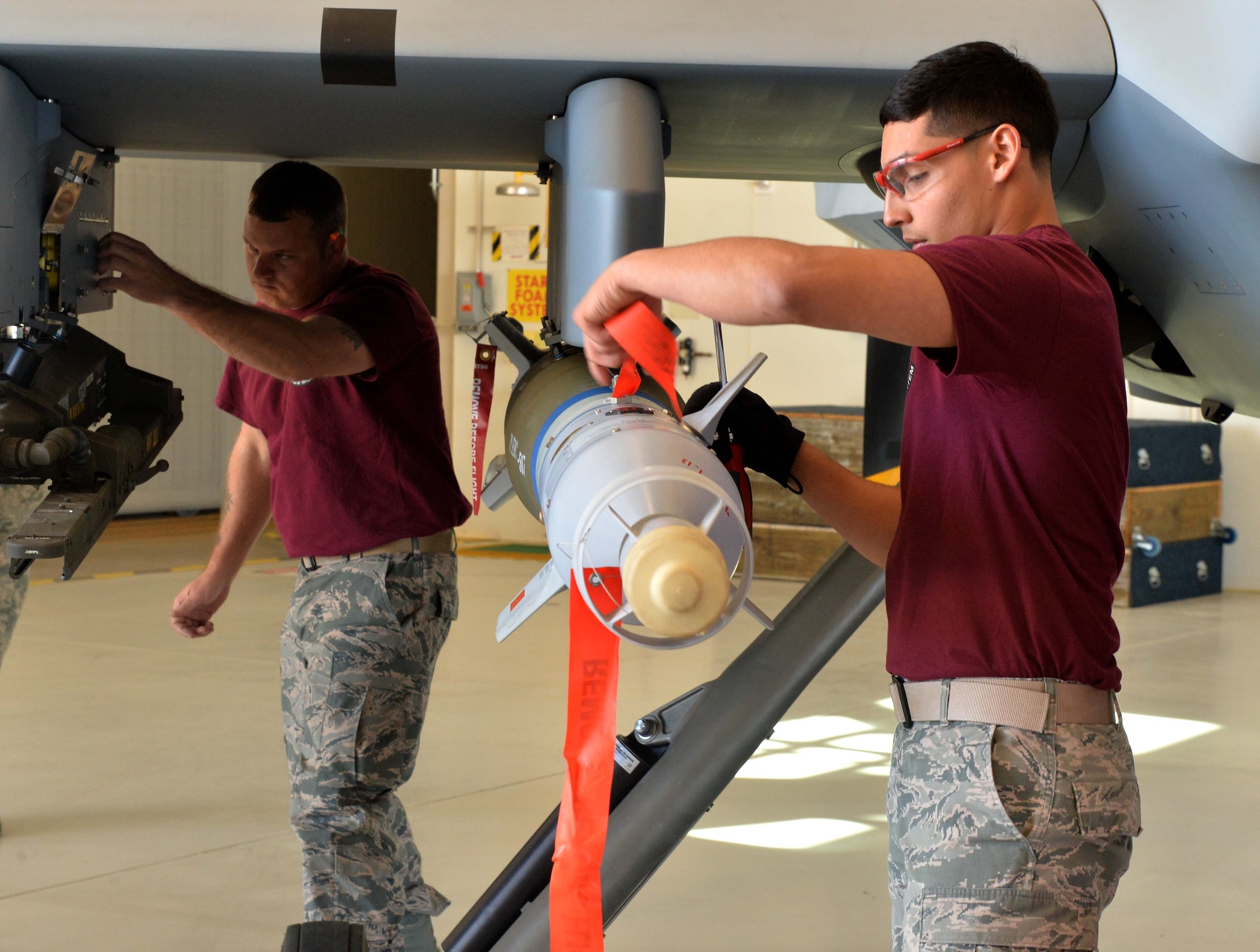 Staff Sgt. Charlie, 432nd Aircraft Maintenance Squadron weapons load crew chief and Airman 1st Class Ricardo, 432nd AMXS weapons load crew member perform maintenance on an MQ-9 Reaper weapons pylon during the Load Crew of the Year competition March 9, 2016, at Creech Air Force Base, Nevada. Charlie and Ricardo are both from crew 25 of Reaper Aircraft Maintenance Unit. (U.S Air Force photo by Airman 1st Class Kristan Campbell/Released)