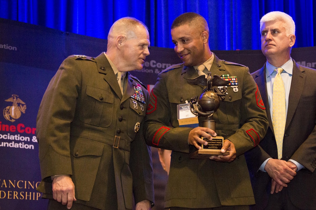 U.S. Marine Corps Staff Sgt. Deacon T. Matthews, center, listens to Commandant of the Marine Corps Gen. Robert B. Neller, left, during the 12th Marine Corps Association and Foundation Ground Logistics Awards dinner at the Crystal Gateway Marriot, Arlington, Va., March 24, 2016. Matthews was awarded the 2015 Marine Corps enlisted logistician of the year. (U.S. Marine Corps photo by Staff Sgt. Gabriela Garcia/Released)