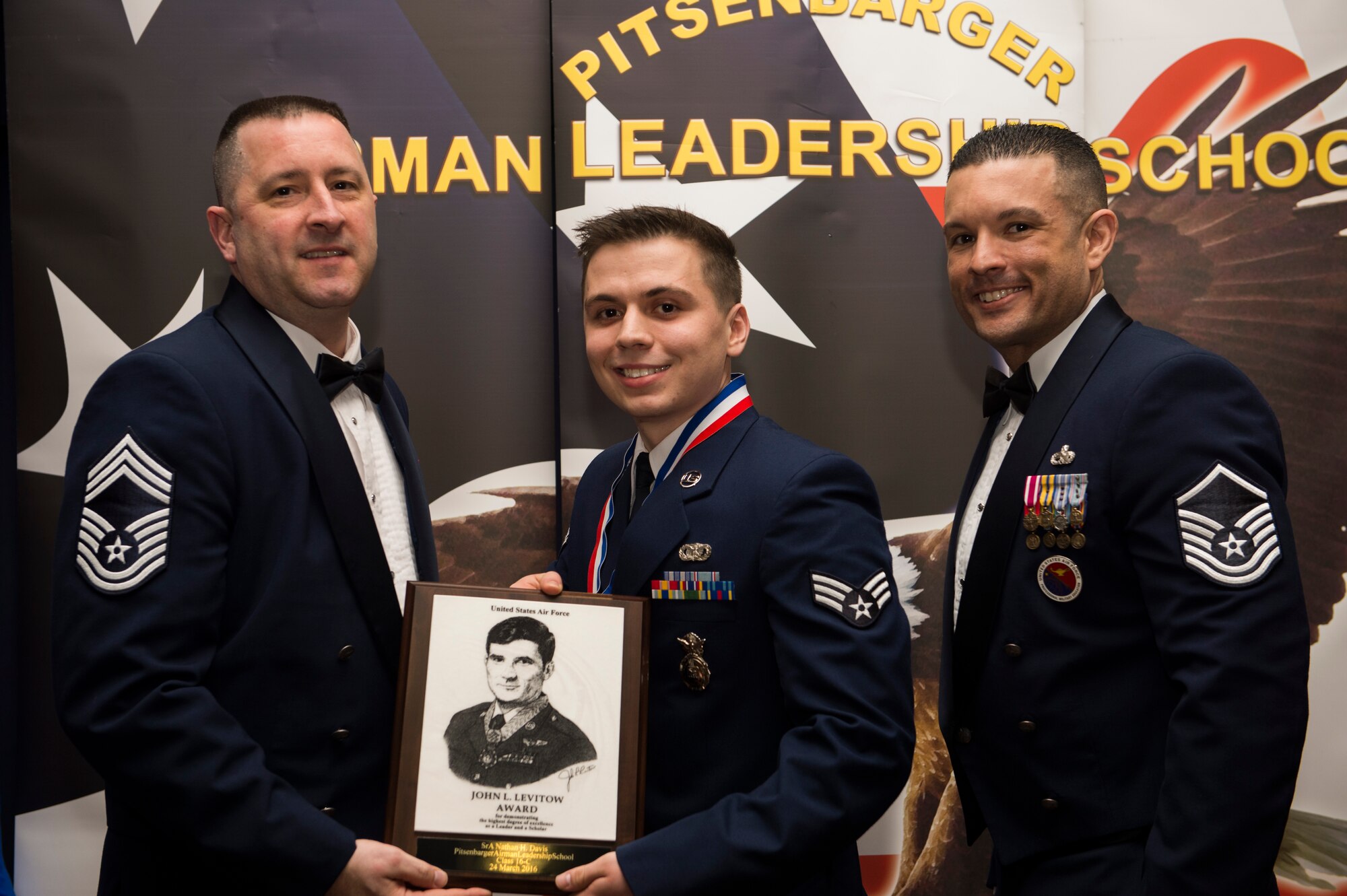 U.S. Air Force Chief Master Sgt. Richard Lukens, 52nd Equipment Maintenance Squadron superintendent, left, and U.S. Air Force Master Sgt. Roberto Oregon, Pitsenbarger Airman Leadership School commandant, right, present U.S. Air Force Senior Airman Nathan Davis, 703rd Munitions Support Squadron, center, with the John L. Levitow award during the ALS Class 16-B graduation ceremony at Club Eifel on Spangdahlem Air Base, Germany, March 24, 2016. The Levitow award is presented to the student who demonstrated the most outstanding leadership and scholastic qualities based on academic performance and assignment of points by peers and instructors. (U.S. Air Force photo by Airman 1st Class Timothy Kim/Released)