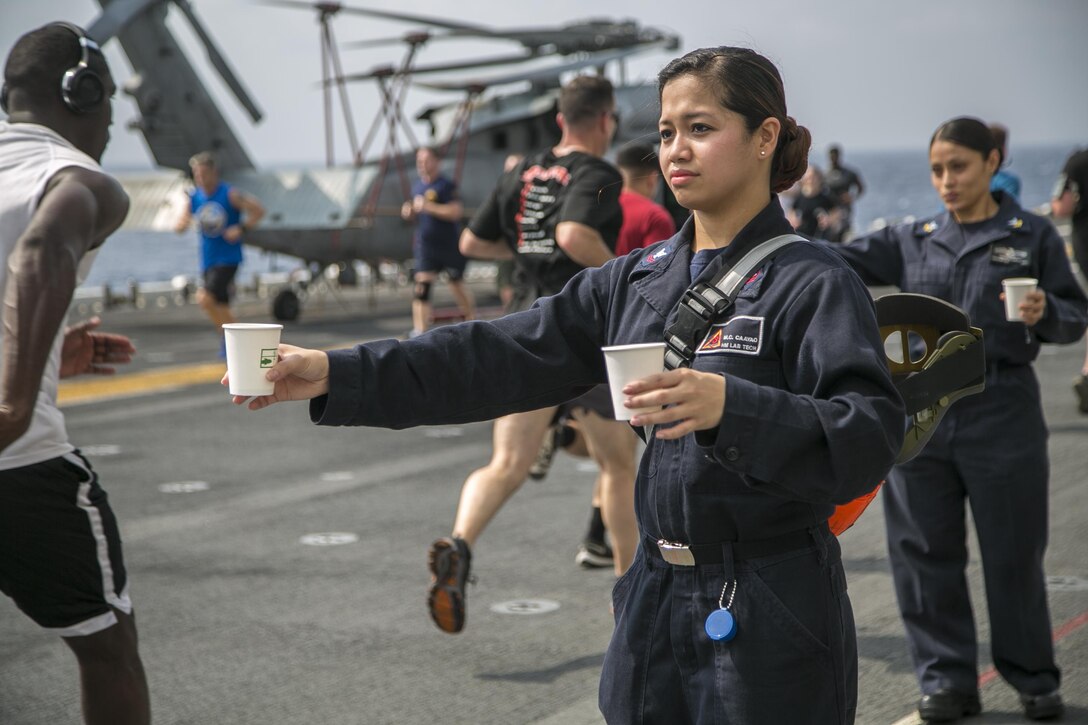 Navy Petty Officer 2nd Class Charissa Caayao hands out water to participants in a Women's History Month 5K run aboard the USS Boxer in the Pacific Ocean, March 27, 2016. Marine Corps photo by Sgt. Briauna Birl