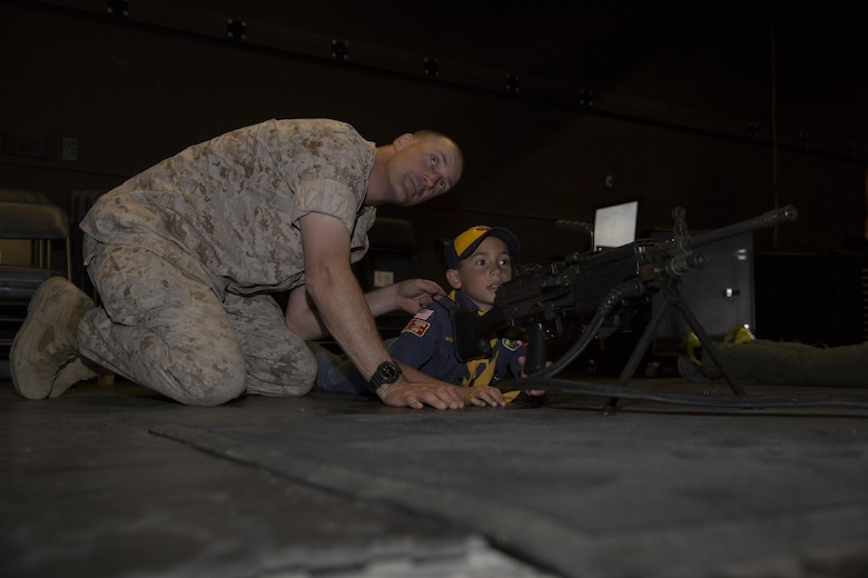 Maj. Jamison Fox, officer in charge, Exercise Logistics Coordination Center, instructs his son, Aiden, 8, cub scout, troop 78, on the operation of the M249 Squad Automatic Weapon at the Indoor Simulated Marksmanship Trainer during the Boy Scout Camp Out for local Boy Scouts of America troops March 18, 2016. (Official Marine Corps photo by Sgt. Charles Santamaria/Released)