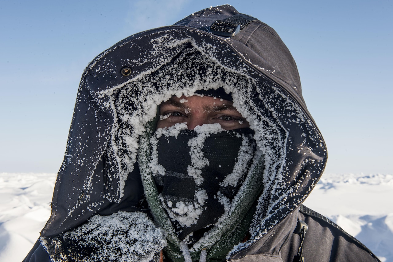 A man’s face is almost obscured by winter clothing and a snow-dusted mask.