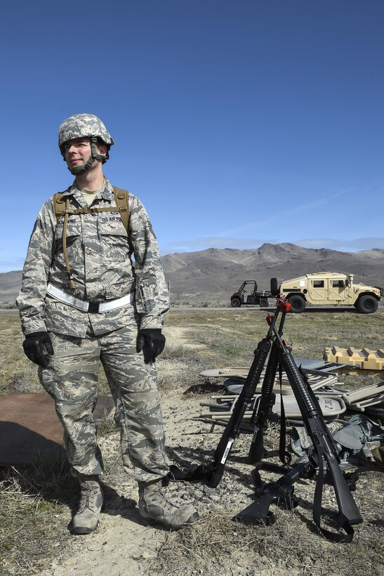 Air Force Tech. Sgt. Brian Thompkins stands next to M16 assault rifles while other airmen and soldiers assemble tents during Exercise Turbo Distribution 16-02 at Amedee Army Airfield, Calif., March 15, 2016. Thompkins is a weather forecaster assigned to the 921st Contingency Response Squadron. Air Force photo by Staff Sgt. Robert Hicks