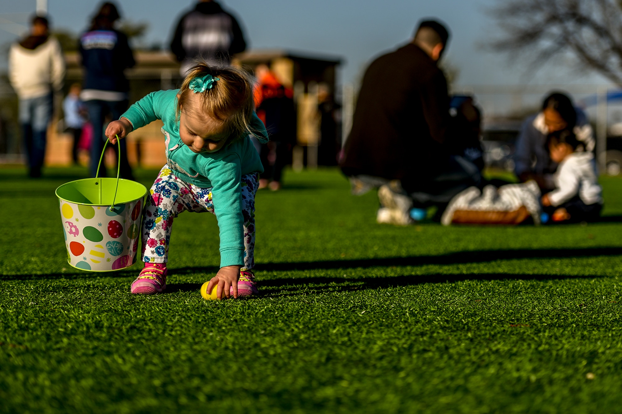 A one-year-old girl picks up an Easter egg at the softball field on Goodfellow Air Force Base, Texas, March 26, 2016. The 17th Force Support Squadron hosted the Easter egg hunt to celebrate the holiday with Goodfellow families. (U.S. Air Force photo by Senior Airman Devin Boyer/Released)