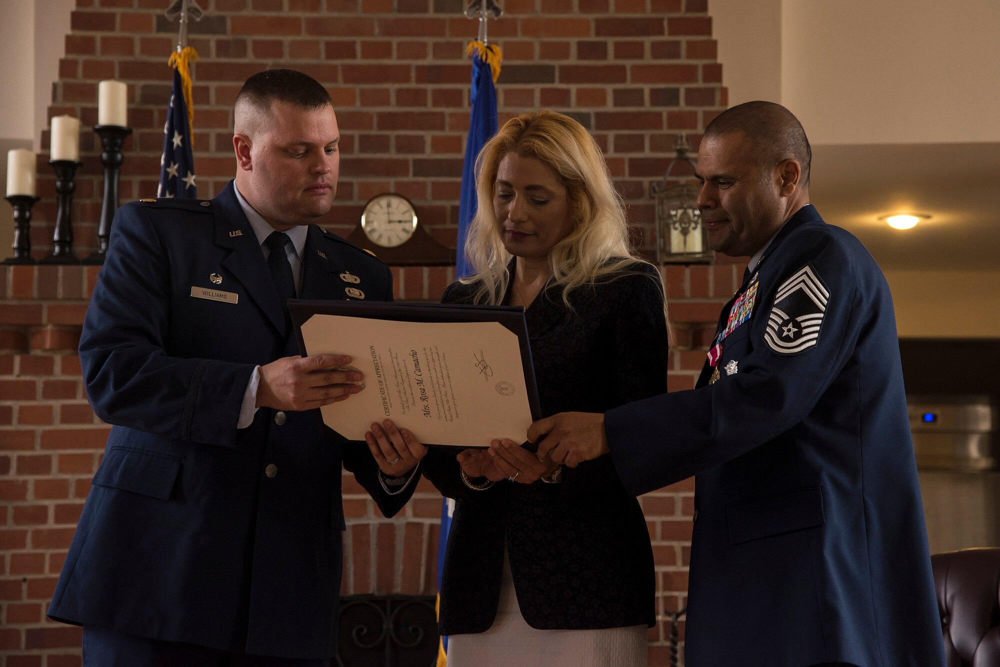 U.S. Air Force Chief Master Sgt. Manuel Camacho, 23d Security Forces Squadron manager, right, and his wife Rose Mary, center, review a certificate of appreciation awarded by Maj. Aaron Williams, 23d Security Forces Squadron commander, during Camacho’s retirement ceremony, March 28, 2016, at Moody Air Force Base, Ga. The couple received several certificates of appreciation during the ceremony for their sacrifices and dedication throughout his 30-year career. (U.S. Air Force photo by Airman 1st Class Janiqua P. Robinson/Released)