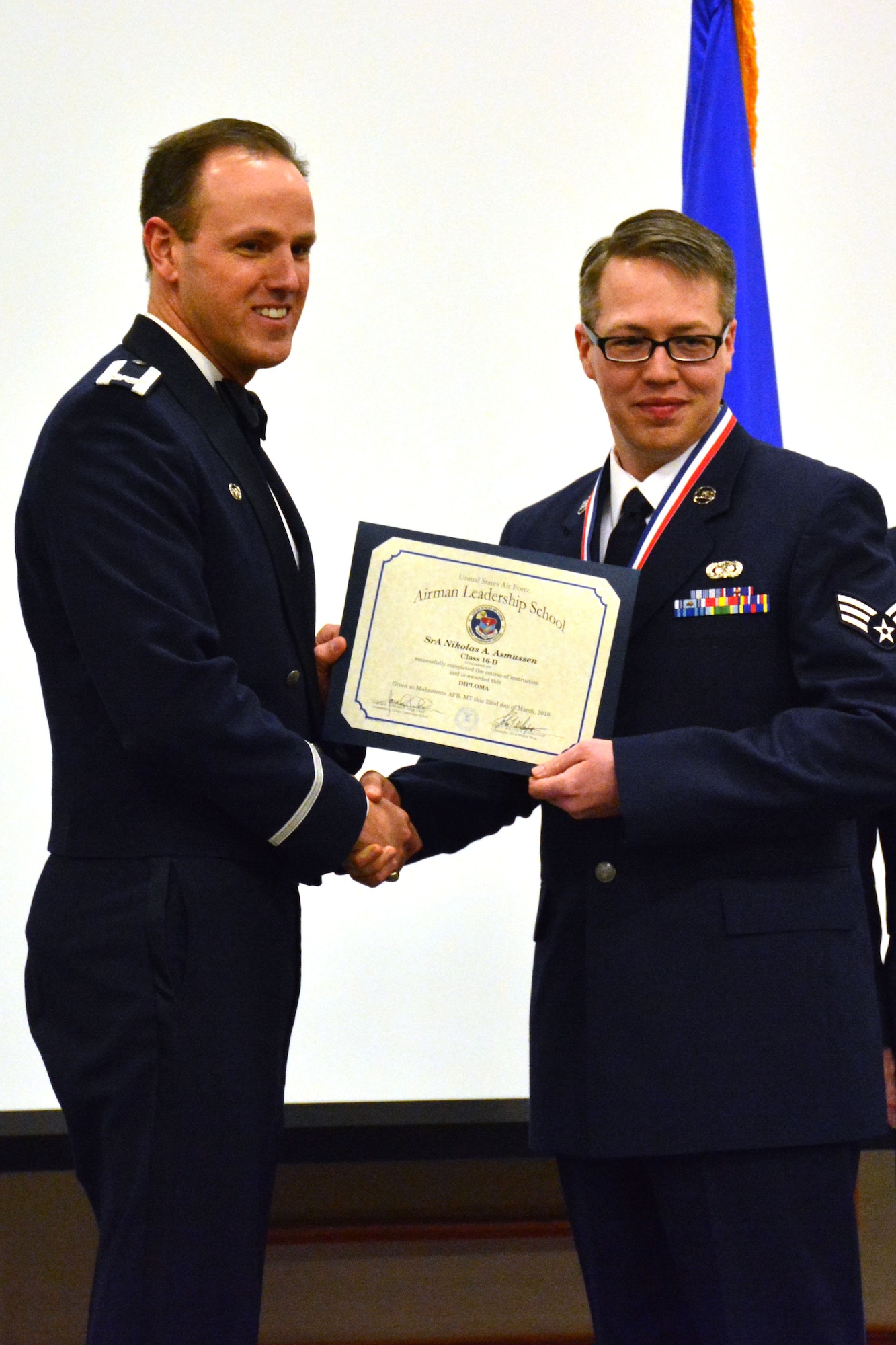 120th Airlift Wing Commander Col. Lee Smith presents an Airman Leadership School diploma to Senior Airman Nikolas Asmussen, March 22, 2016. Asmussen was one of 32 students who graduated from ALS class 16-D at Malmstrom Air Force Base, Mont. (U.S. Air National Guard photo by Senior Master Sgt. Eric Peterson)