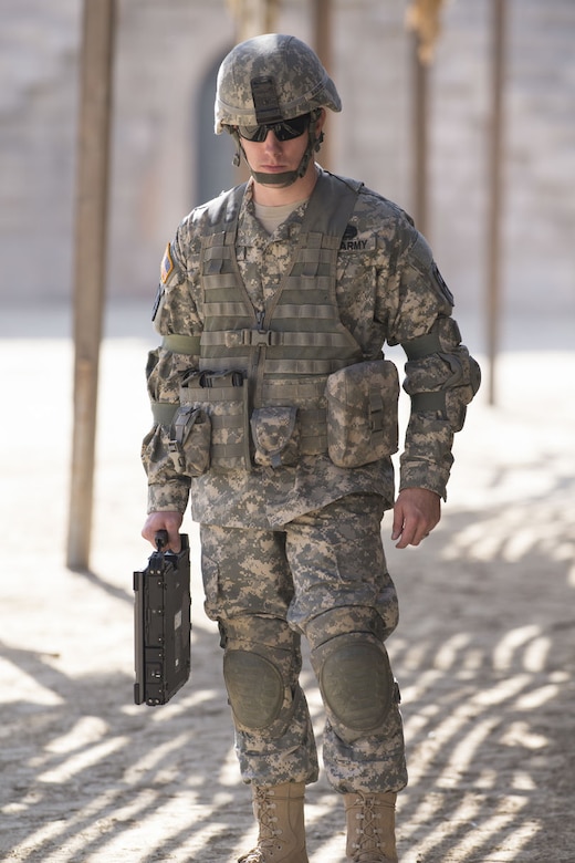 Army Soldier signal support systems specialist wearing ACU holding laptop outside during the day.
