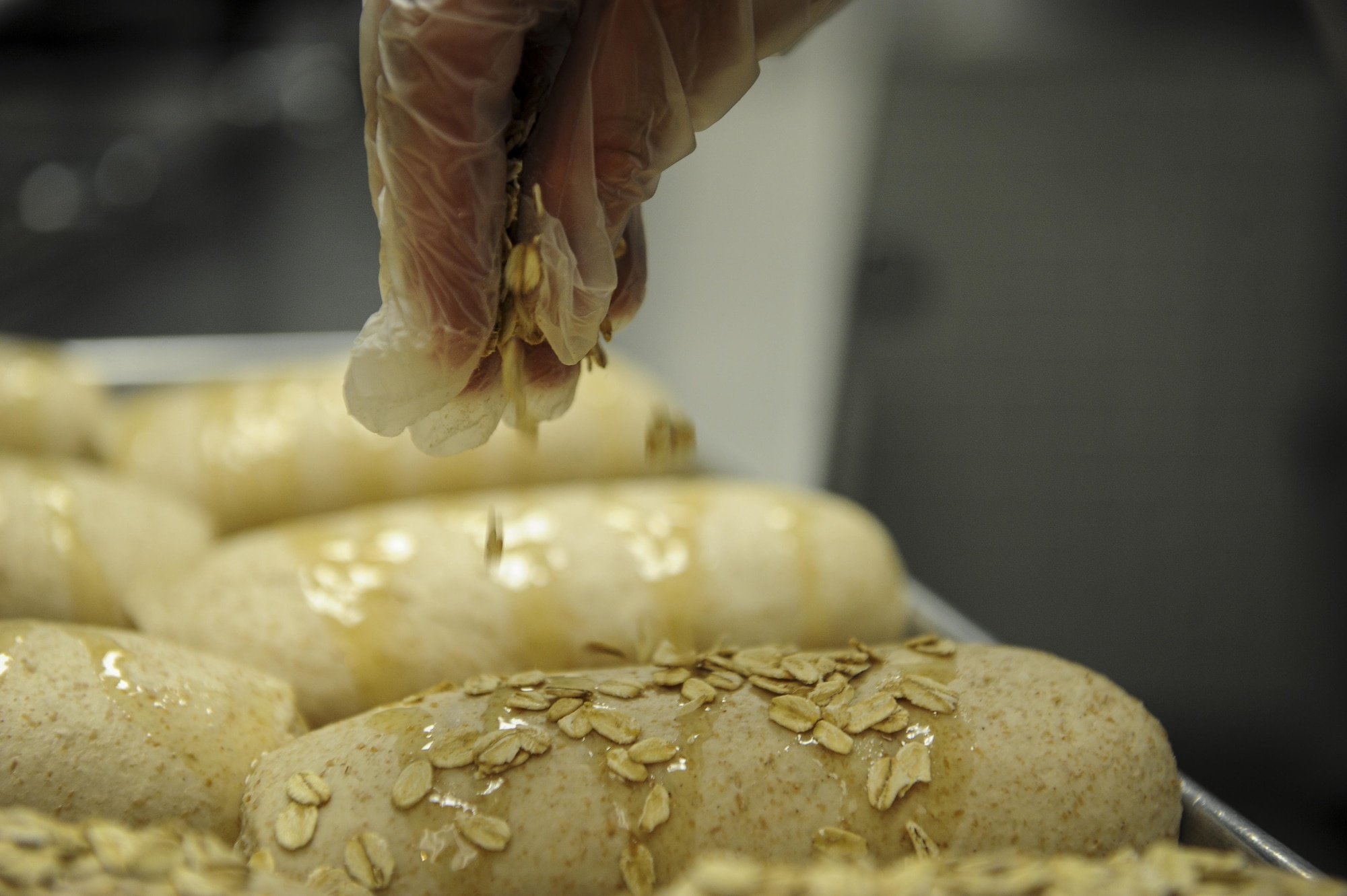 Airman 1st Class Tyler Aguilar, a food service journeyman with the 1st Special Operations Force Support Squadron, sprinkles oats on bread to be baked at Hurlburt Field, Fla., March 28, 2016. Aguilar is The Reef dining facility’s food preparation cook, in charge of preparing the meat and bread served. (U.S. Air Force photo by Senior Airman Meagan Schutter)