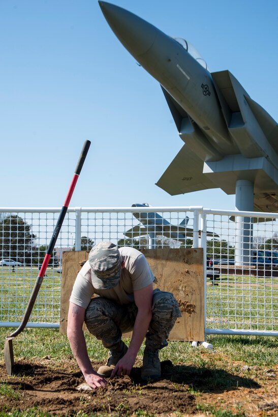 U.S. Air Force Airman Quindon Clark, a heavy equipment operator assigned to the 633rd Civil Engineer Squadron, flattens dirt around a polyvinyl chloride pipe to create a new flag post hole at Langley Air Force Base, Va., March 16, 2016.The holes are three feet deep and two feet wide, which provides enough support for the new flag post to withstand possible strong hurricane winds. . (U.S. Air Force photo by Staff Sgt. J.D. Strong II)