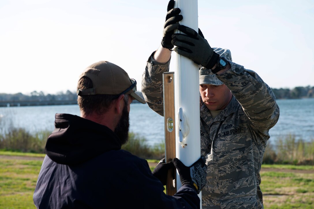 U.S. Air Force Tech. Sgt. Brandon Bridges, a structural craftsman assigned to the 633rd Civil Engineer Squadron, holds a new flag post while Geoff Hauser, a structural craftsman assigned to the 633rd CES, checks a hand-held level at Memorial Park at Langley Air Force Base, Va., March 24, 2016. The CES installed new flag posts at Memorial Park that can withstand possible hurricane-strength winds. (U.S. Air Force photo by Airman 1st Class Derek Seifert) 