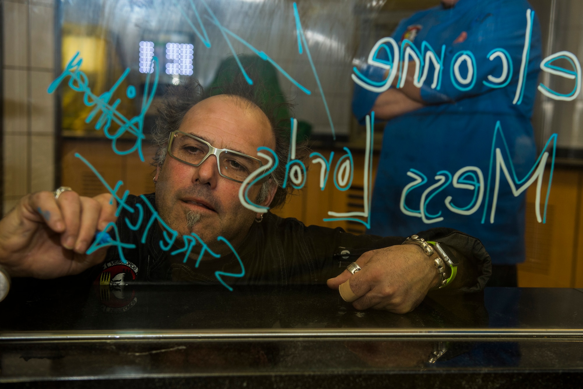 Stretch, a Messlords member, signs his name on a piece of glass at the Mosel Dining Facility at Spangdahlem Air Base, Germany, March 30, 2016. Stretch, owner of ‘Grinders’ restaurants in Kansas City, Mo., is one of four original Messlords and has been providing service members meals  through the tour for seven consecutive years. (U.S. Air Force photo by Senior Airman Luke Kitterman/Released)