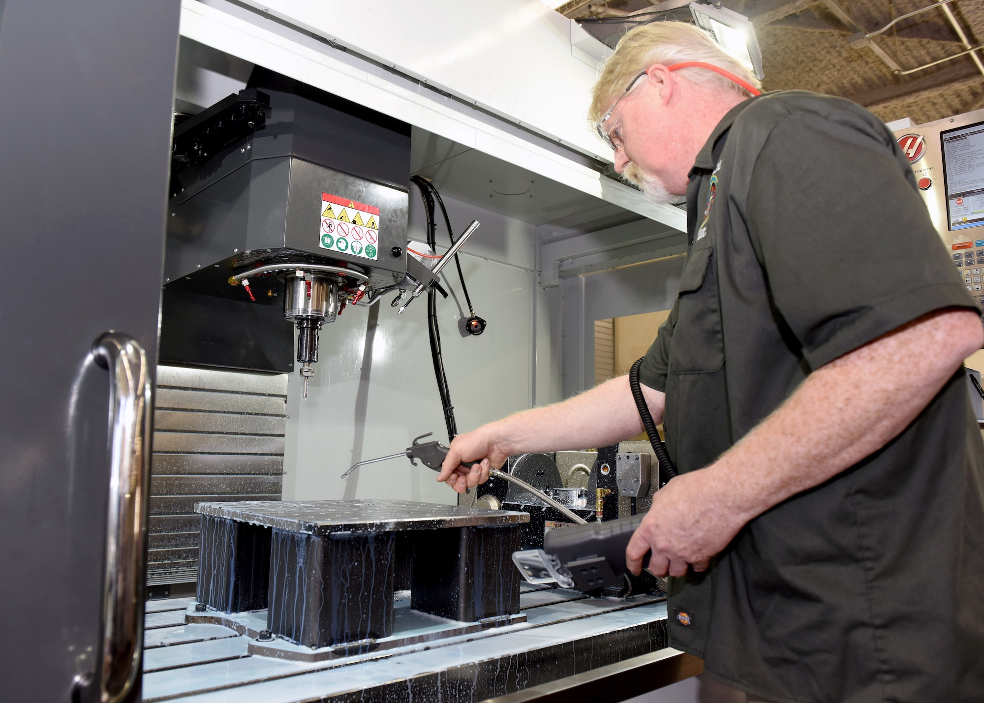 Joaquin Tinker, 30th Operations Support Squadron Training Device Design and Engineering Center mechanical engineering technician, hoses off a device after a Computer Numerical Controlled Milling Center completed its cutting operation, May 26, 2016, Vandenberg Air Force Base, Calif. Undertaking their own machining, electronics, carpentry, painting, 3-D printing and more – each individual at the TDDEC is a specialist in nearly 35 different trades. (U.S. Air Force photo by Senior Airman Kyla Gifford/Released)