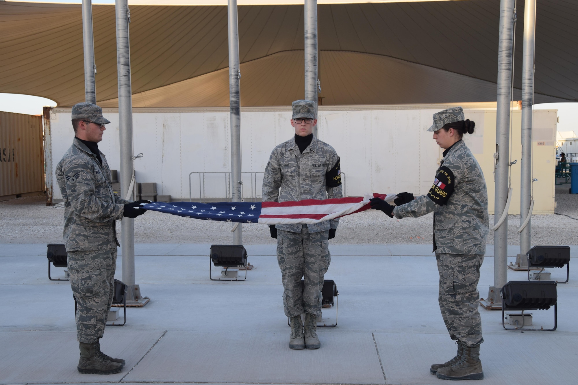Al Udeid Air Base Honor Guard member Senior Airman Travis Huhn (center) prepares to receive the Colors as fellow Honor Guard members Senior Airman Brianna Walberg (right) and Senior Airman Randy Willis (left) fold the flag during the “Days of Remembrance” observance retreat ceremony at Al Udeid AB, Qatar May 1, 2016. (U.S.  Air Force photo by Technical Sgt. Carlos J. Trevino/Released)