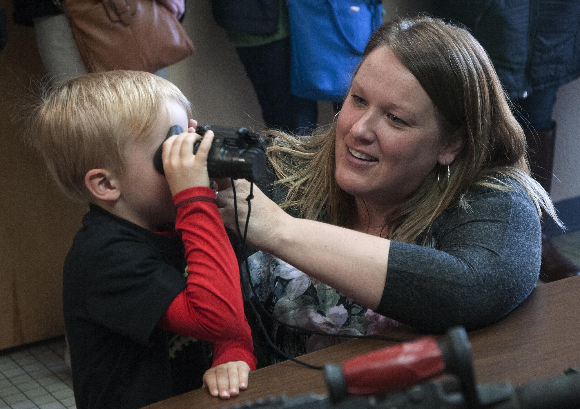 Deanna Flint, wife of Col. Trevor Flint, 90th Maintenance Group commander, helps her son, Will, 5, look through a pair of night vision goggles May, 2, 2016, during the 90th Security Forces Group spouse’s appreciation week event inside the 90th SFG Military Working Dogs facility. Security Forces combat arms trainers showed spouses and children the weapons and gear Mighty Ninety Airmen use to complete their security mission. (U.S. Air Force photo by Senior Airman Brandon Valle)